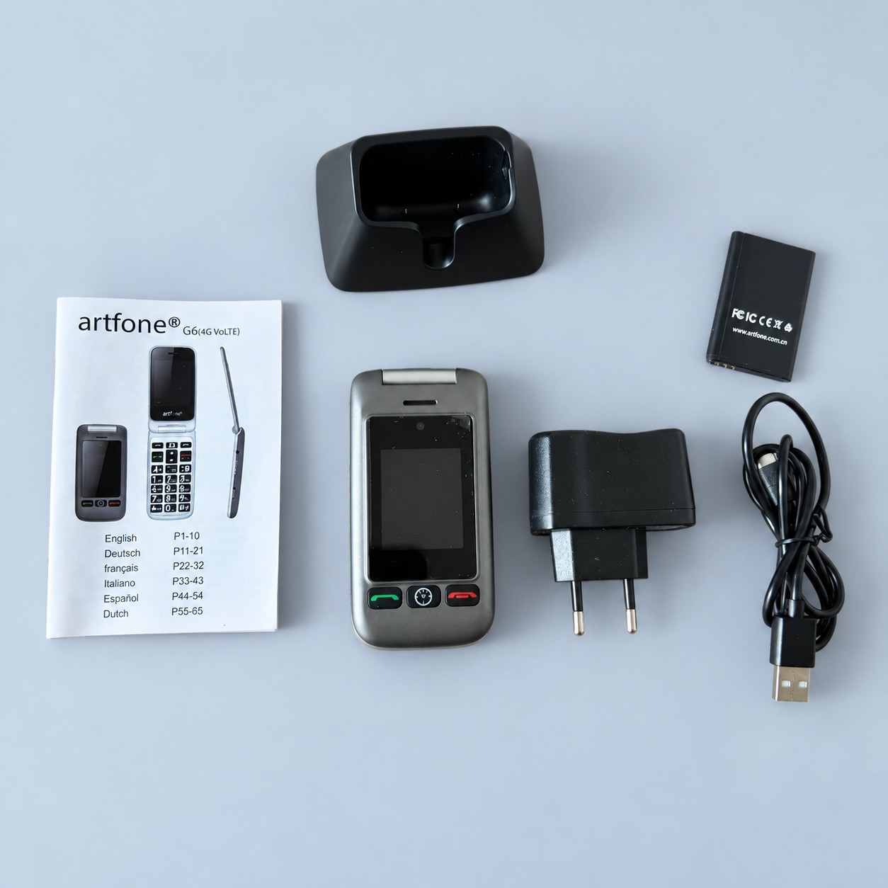 Szary telefon z klapką i akcesoriami — aranżacja poglądowa AI na szaroniebieskim tle