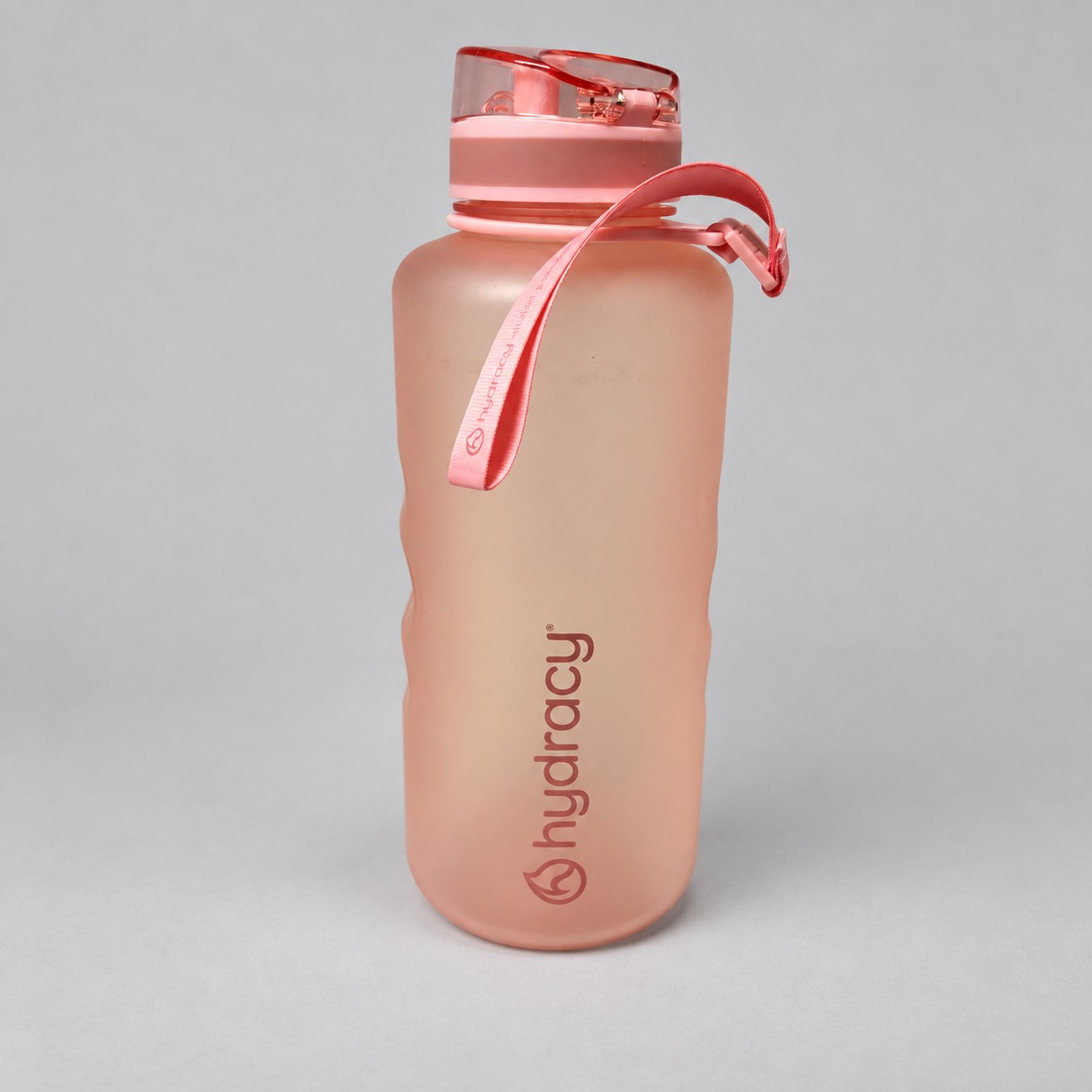 Różowa butelka Hydracy — aranżacja poglądowa AI na szaroniebieskim tle