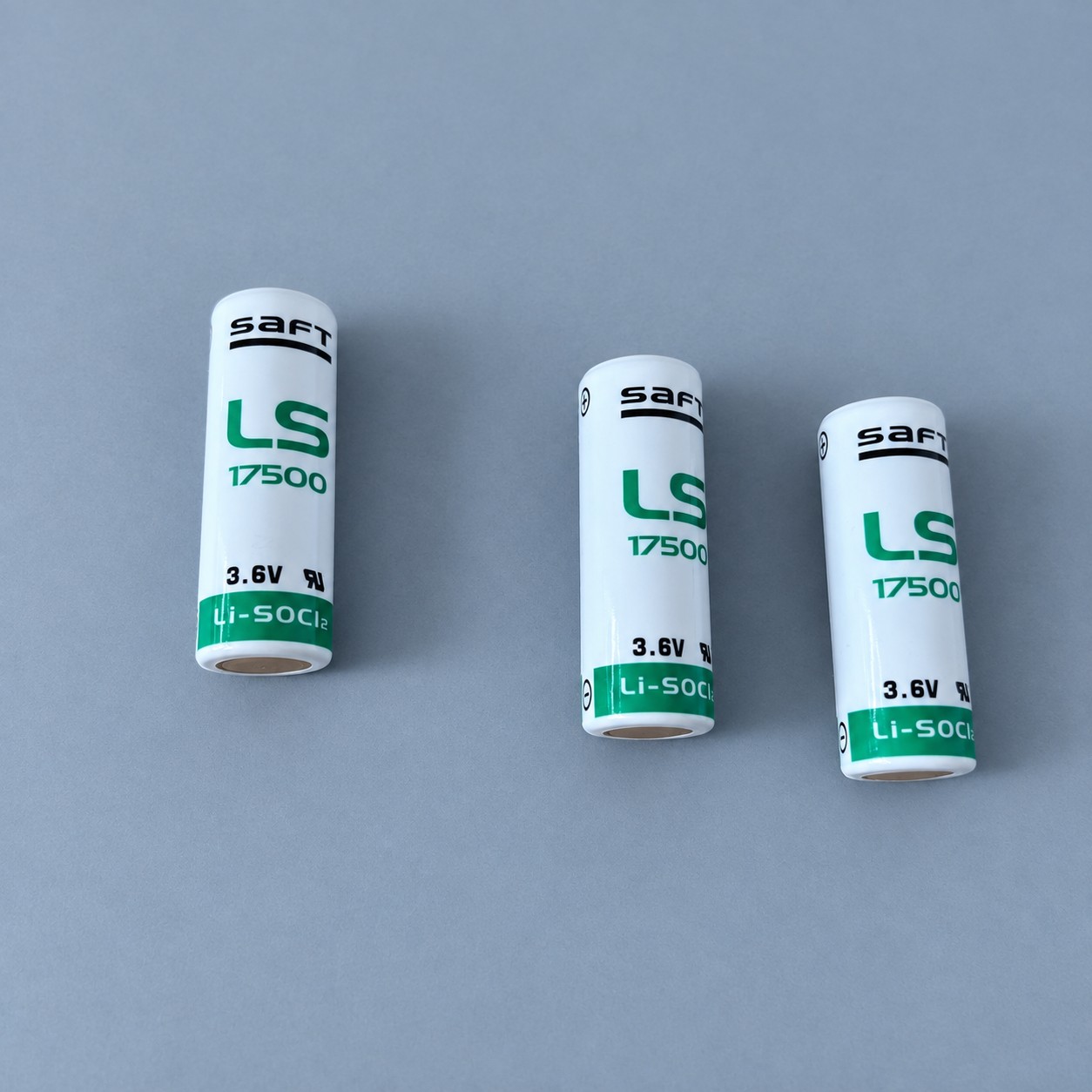 Trzy baterie Saft LS17500 — aranżacja poglądowa AI na szaroniebieskim tle