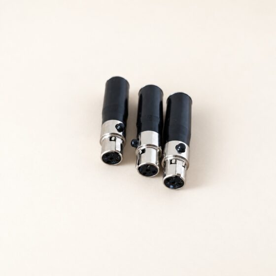 Trzy adaptery audio XLR na kremowym tle.