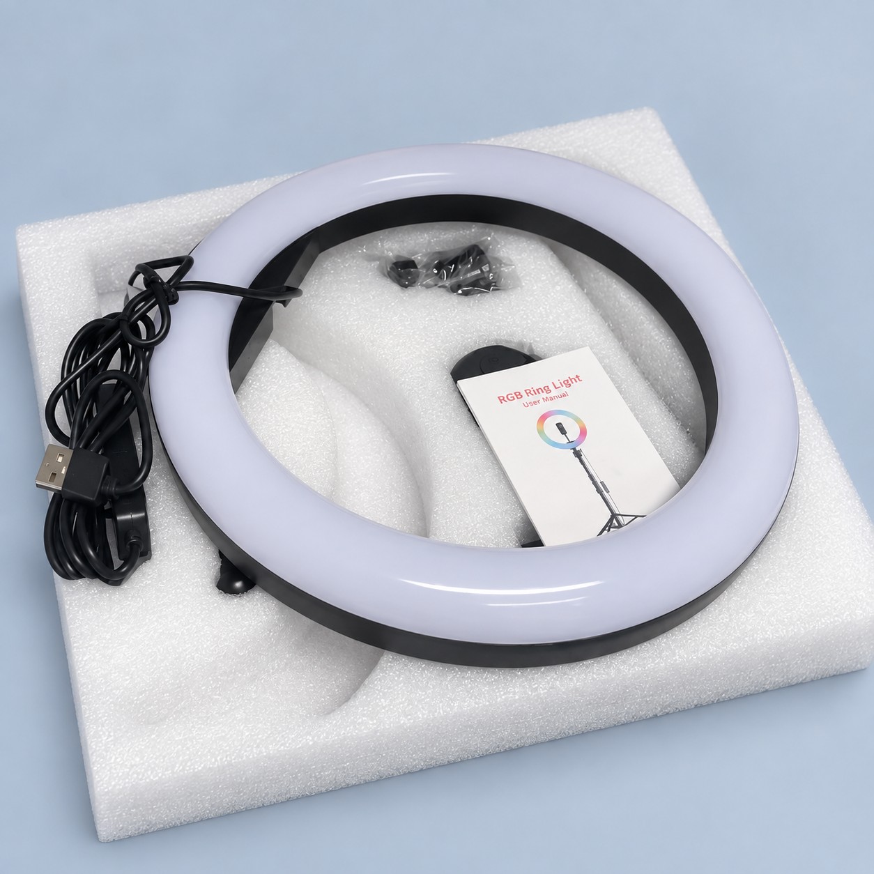 Lampa pierścieniowa Ring LED RGB ze statywem i pilotem — aranżacja poglądowa AI na szaroniebieskim tle